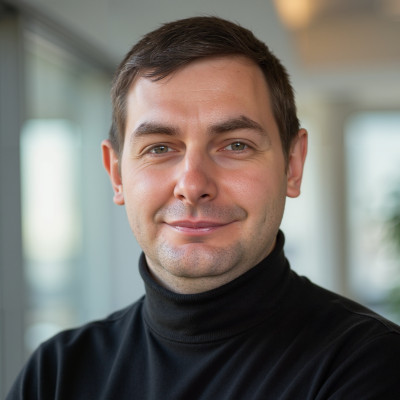 InspireHM— A man with short brown hair, wearing a black turtleneck sweater, stands indoors with a soft smile. The background is softly blurred with natural light coming through windows.